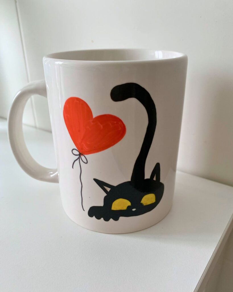 Taza personalizada con dibujo de gatito negro sujetando un globo en forma de corazón